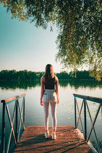 Rear view of woman standing by railing against lake