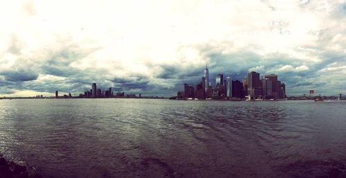 City at waterfront against cloudy sky