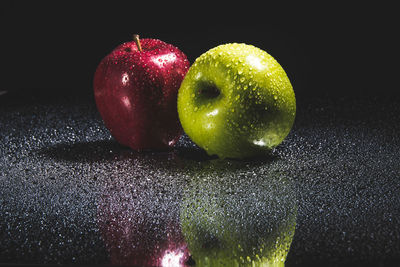 Close-up of wet apple on table against black background