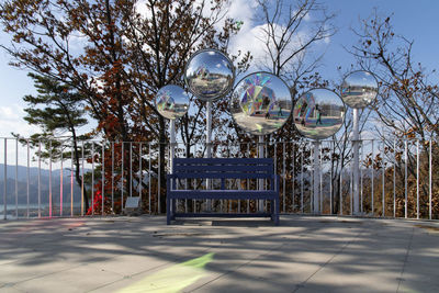 Curved mirrors behind bench in park against sky
