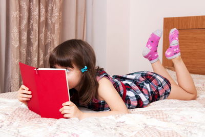Young woman using digital tablet while lying on bed at home