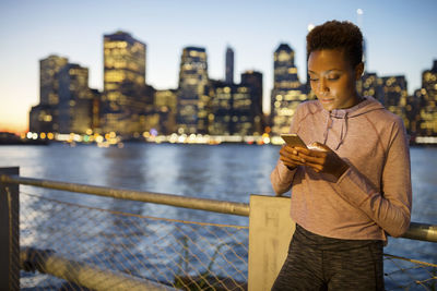 Athlete using mobile phone while standing against illuminated city