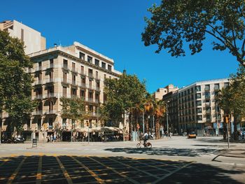 Man cycling on road in city against clear blue sky