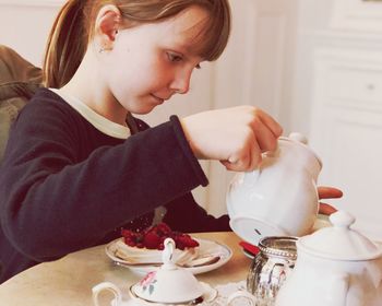 Cute girl pouring tea from kettle at home