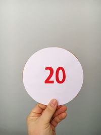 Cropped hand of person holding number on cardboard against gray background