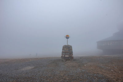 Cross on land by building against sky