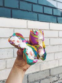 Cropped hand holding colorful sweet food against wall