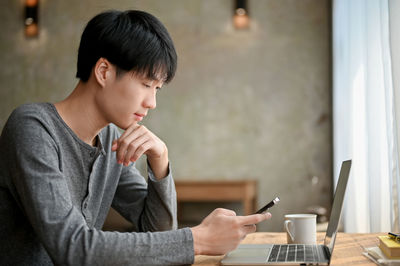 Side view of young woman using laptop at home