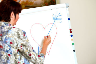 Rear view of woman drawing heart shape on whiteboard