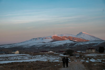 Rear view of man standing on mountain against sky during sunset