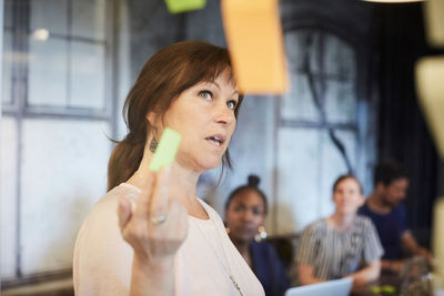 Businesswoman discussing ideas with colleagues over adhesive notes in board room