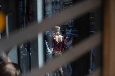 Rear view of woman walking on street seen through window