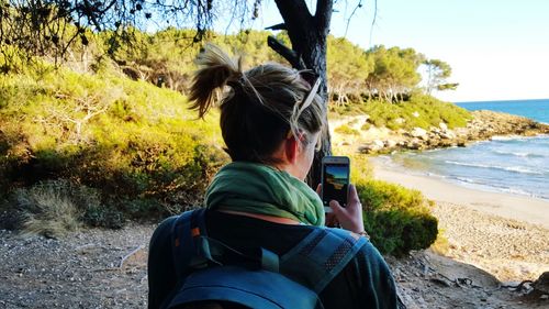 Rear view of woman photographing at beach with smart phone