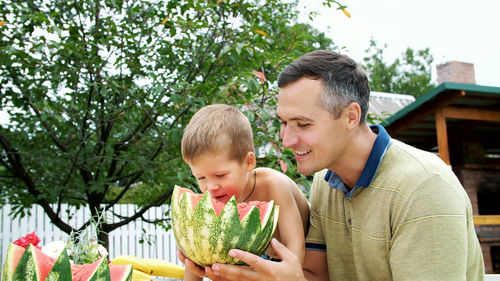 In summer, in the garden, father with a four-year-old son cut a watermelon and eat it, have fun, a