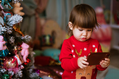 Little girl child playing mobile phone in red christmas sweater next to festive