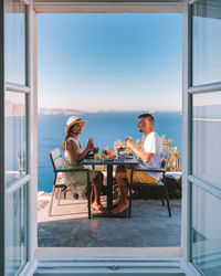 People sitting by swimming pool against window