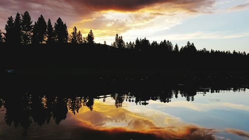 Reflection of silhouette trees in lake against sky during sunset