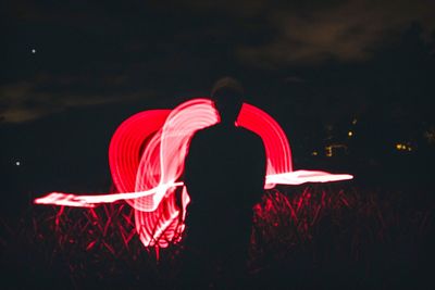 Rear view of man standing against illuminated sky at night