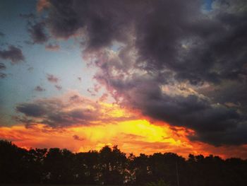 Low angle view of silhouette trees against dramatic sky