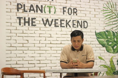 Young man using mobile phone against wall