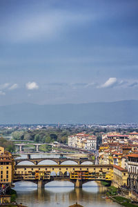 Bridge over river amidst buildings in city against sky