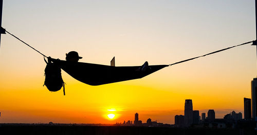 Silhouette person using laptop on hammock at sunset