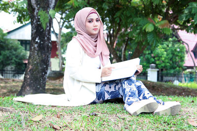 Portrait of smiling young woman reading book while sitting at park