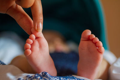 Cropped mother hand holding baby leg on bed at home