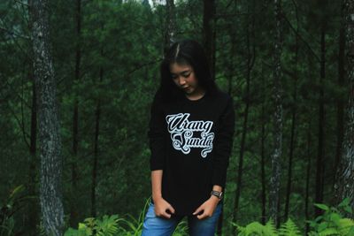 Young woman standing by tree in forest