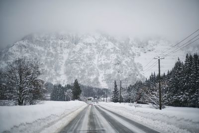 Snow covered road by trees against sky