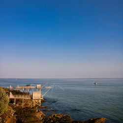 Scenic view of sea and fishing huts against clear blue sky