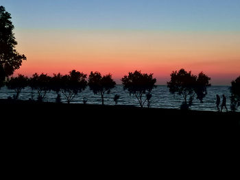 Silhouette trees by sea against sky during sunset