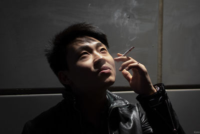 Close-up of man smoking while standing against wall