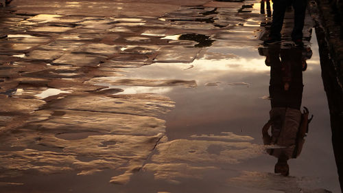 Reflection of man on puddle at street during sunrise