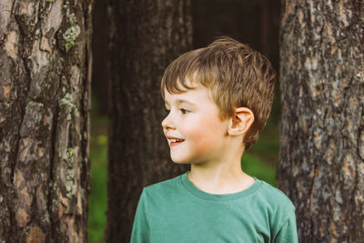 Cute boy looking away standing against tree trunk