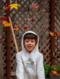 Portrait of cute girl throwing leaves standing outdoors during autumn