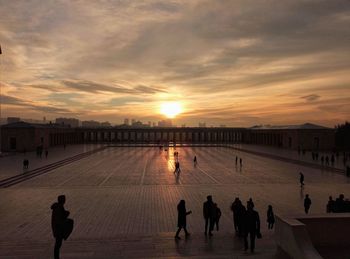 Silhouette people in city against sky during sunset