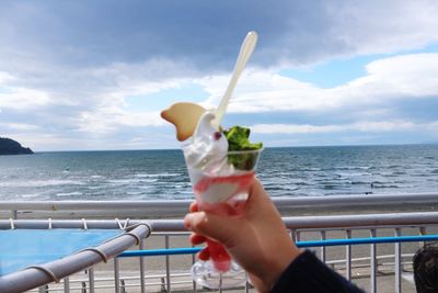 Cropped image of hand holding ice cream against sea