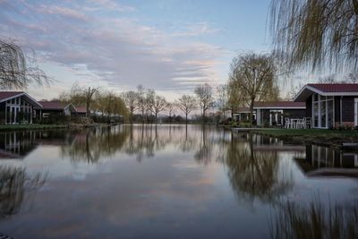Reflection of trees and houses in lake against sky