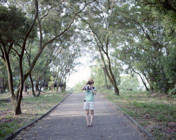 Woman photographing amidst trees on footpath at park