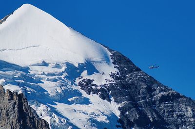 Scenic view of snowcapped mountains against clear blue sky and a helicopter 