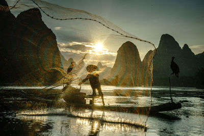 Silhouette fisherman with fishing net in boat on sea during sunset