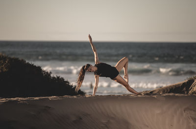 Woman exercising at beach against sky