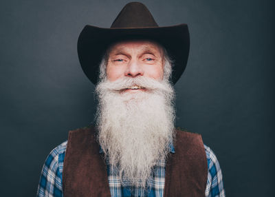 Portrait of happy bearded senior man wearing cowboy hat on gray background