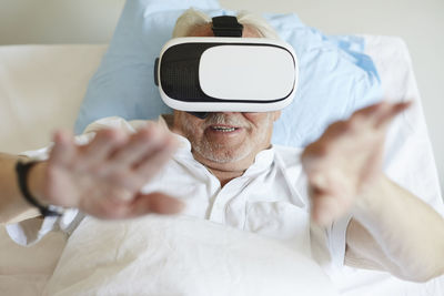 High angle view of senior man gesturing while using vr glasses on bed in hospital ward
