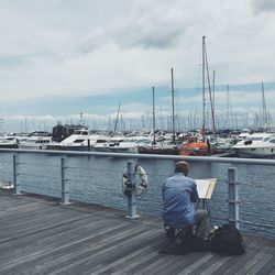 Rear view of man sitting on pier at harbor