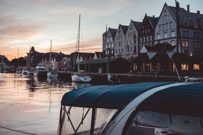 Sailboats moored on canal by buildings against sky during sunset