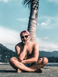 Man wearing sunglasses sitting on mountain against sky