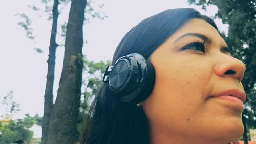 Close-up of woman listening music on headphones against trees