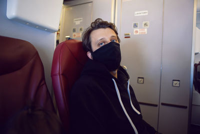 Man in a black jacket with mask is a passenger of the plane sitting on a chair